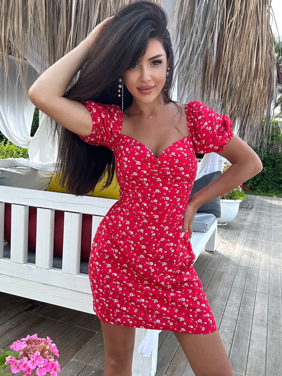 Woman in a red floral dress standing outdoors on a wooden deck.