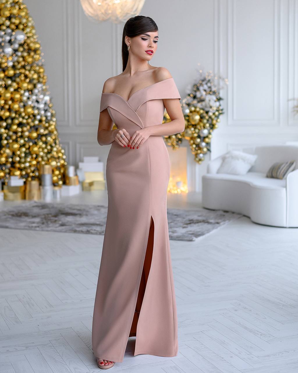 Woman in a long, off-shoulder dress standing in a decorated room with Christmas trees.