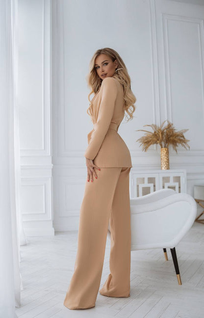 Woman in a beige outfit standing in a stylish room with white walls and decor.
