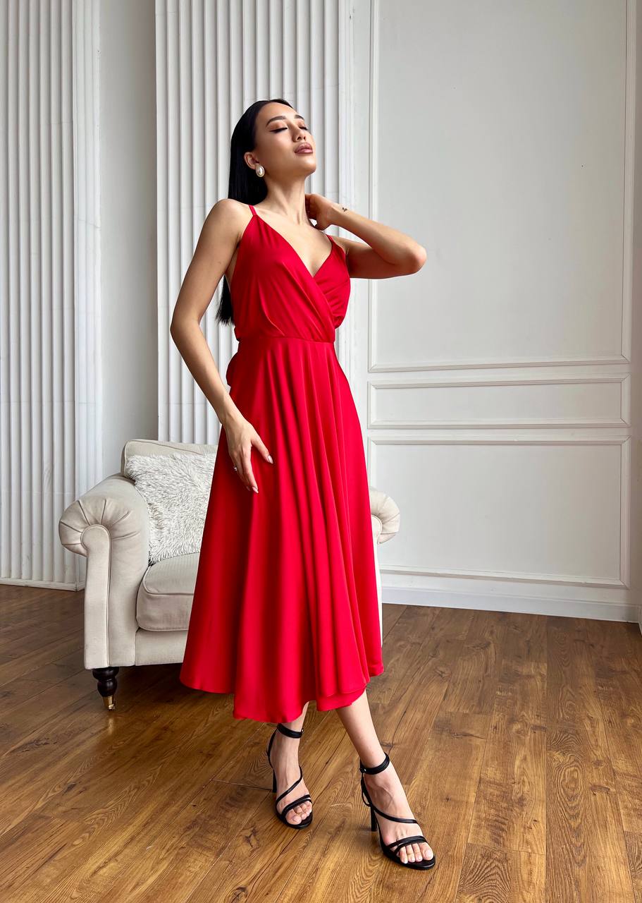 Woman in a red dress standing in a room with wooden floor and white walls.