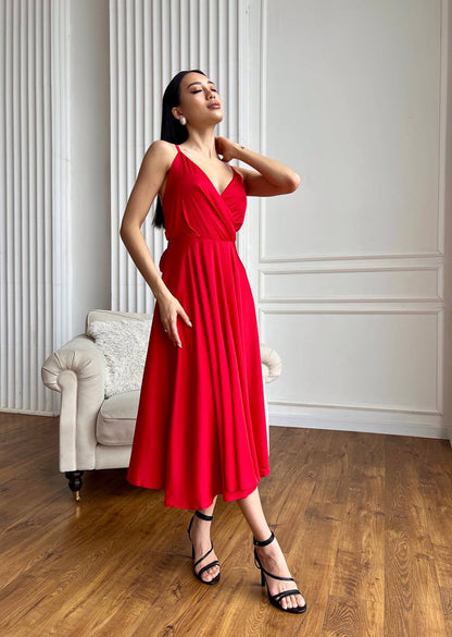 Woman in a red dress standing in a room with wooden floor and white walls.