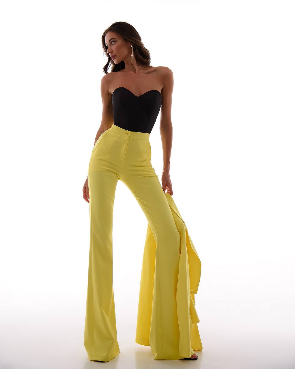 Woman wearing a black strapless top and yellow high-waisted pants on a white background