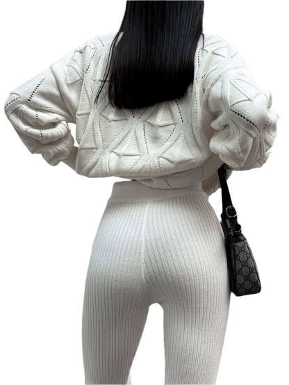 Person wearing a white knit outfit with a black handbag on a white background