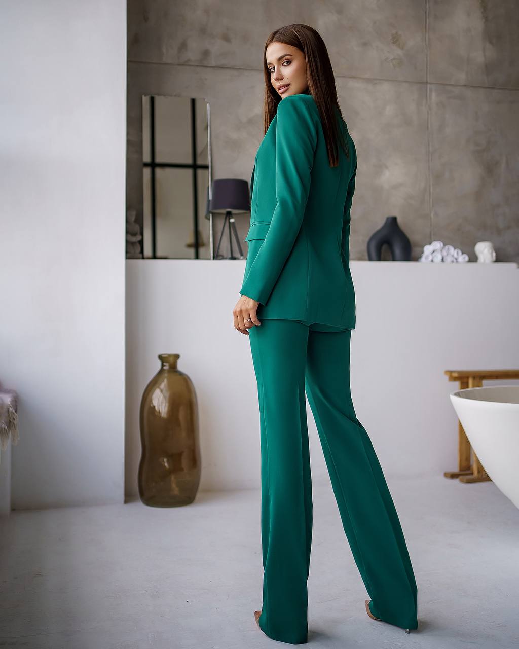 Woman in a teal suit standing in a modern interior setting with neutral colors.