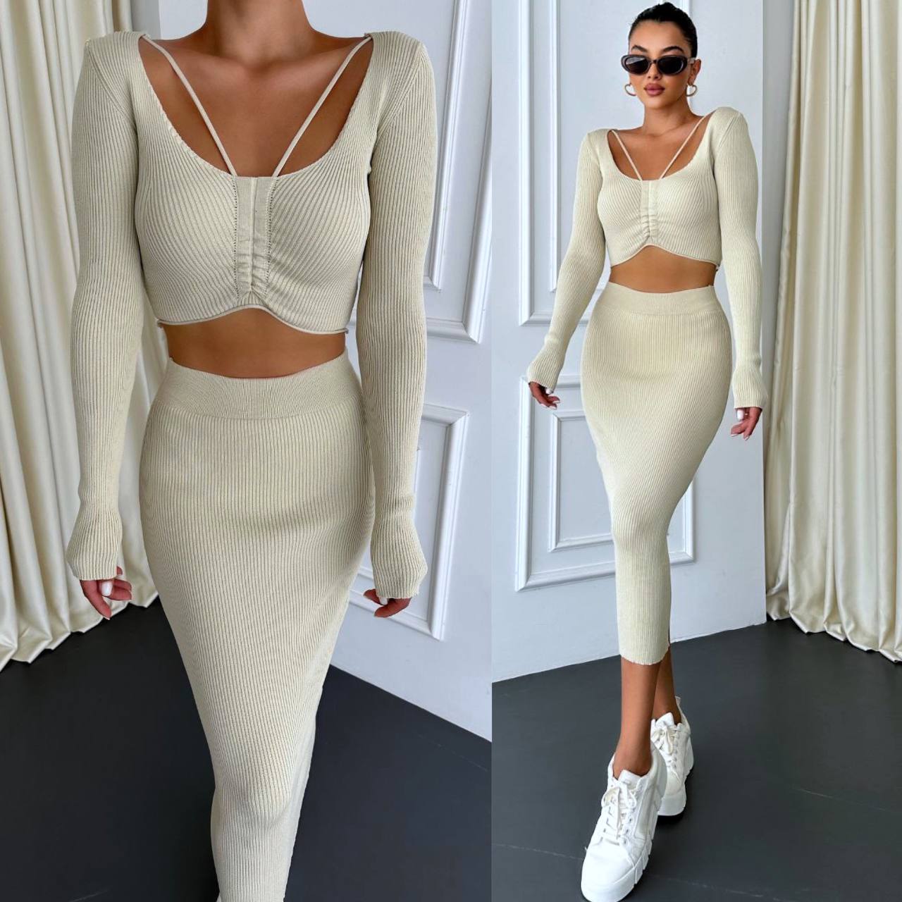 Woman wearing a cream-colored knit outfit with long sleeves and a skirt, standing against a white wall.
