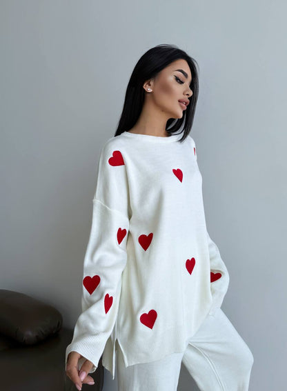 Woman wearing a white sweater with red heart patterns against a plain background
