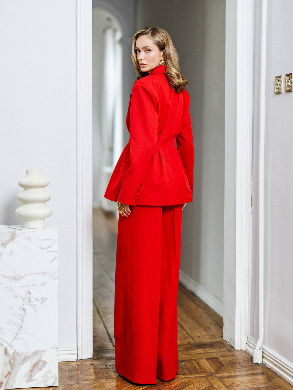 Woman in a red outfit standing in a room with white walls and wooden floor.