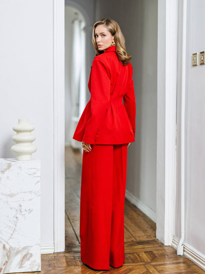 Woman in a red outfit standing in a room with white walls and wooden floor.