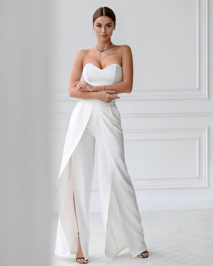 Woman wearing a white strapless jumpsuit with a high slit on a plain background
