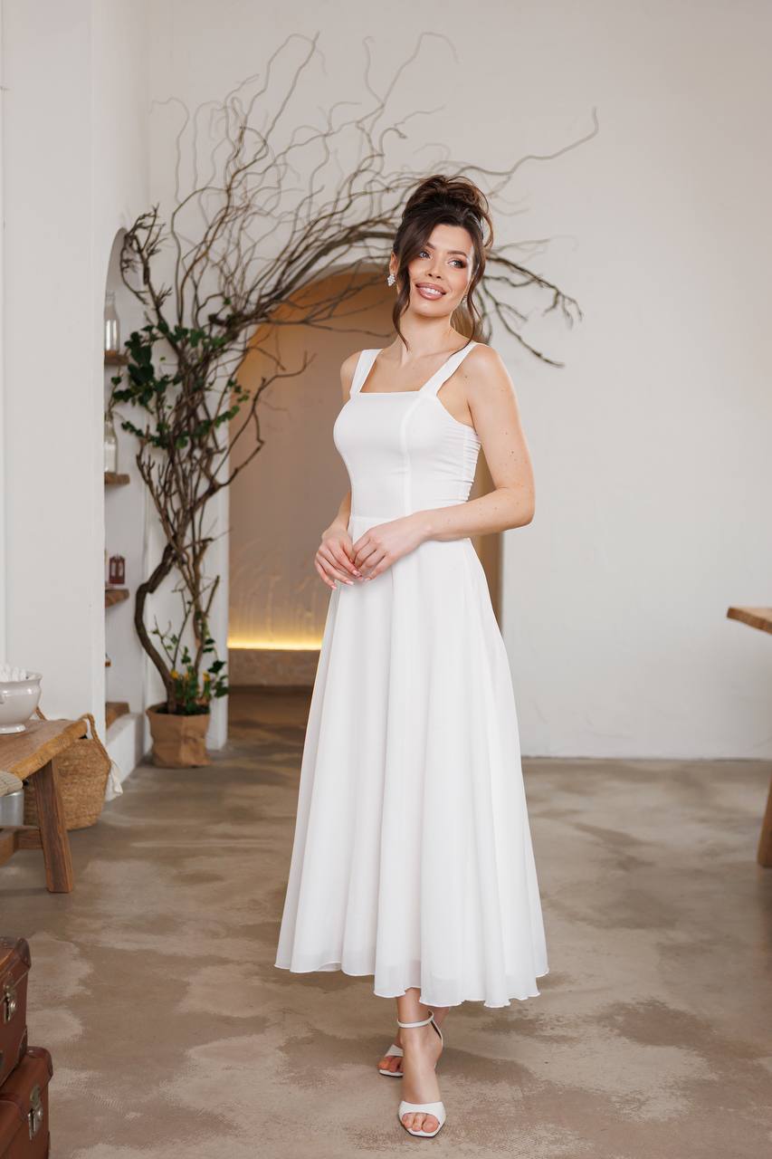 Woman in a white dress standing in an indoor setting with decorative plants.