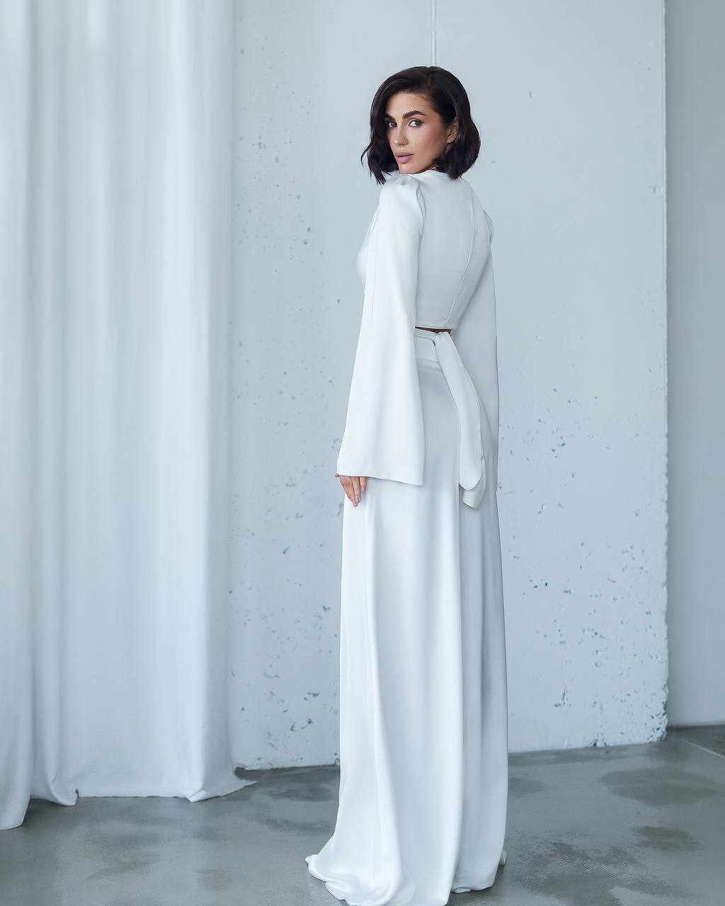 Woman wearing a white outfit standing against a light gray wall.