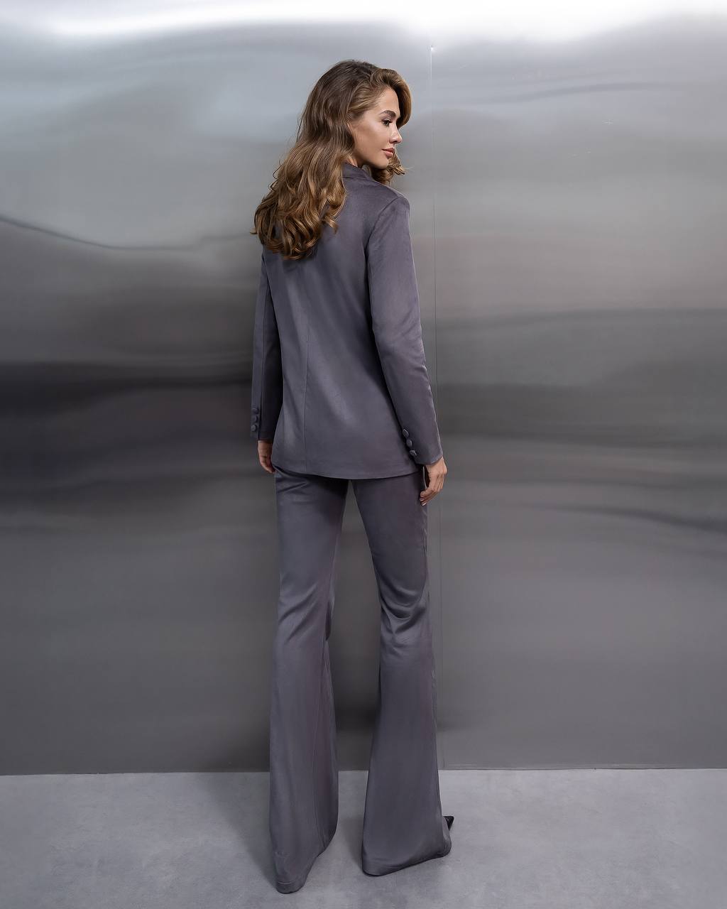 Woman wearing a gray suit with flared pants against a plain background