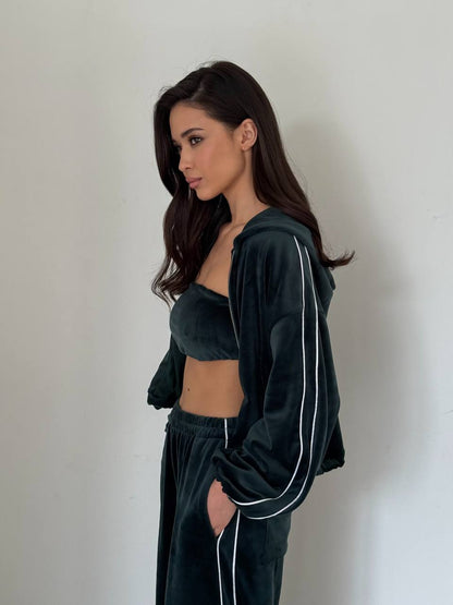 Woman wearing a dark green tracksuit with white stripes against a plain background