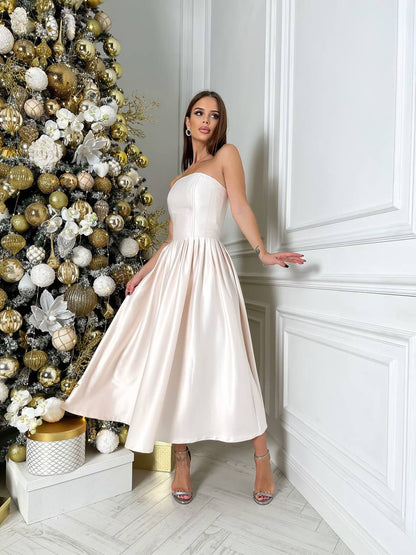 Woman in a white strapless dress standing next to a decorated Christmas tree.