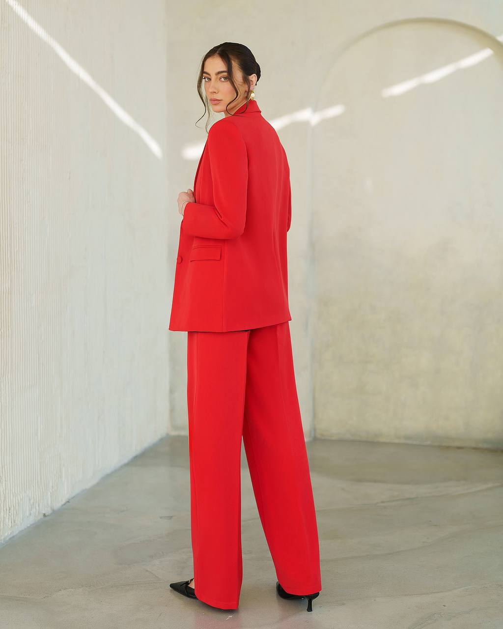 Person wearing a red suit standing in a minimalistic room with white walls and gray floor.