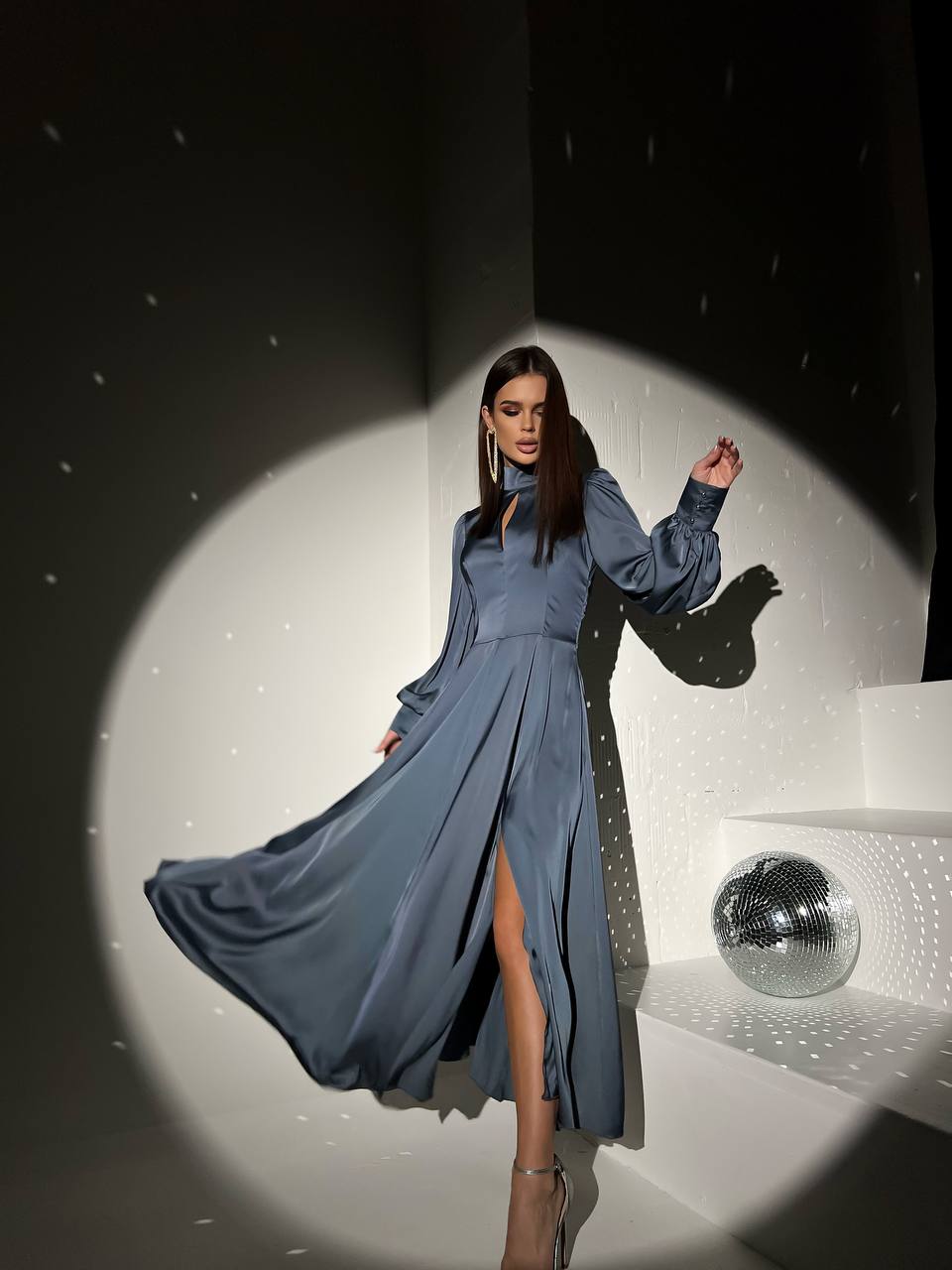 Woman in a blue dress posing on a stage with a disco ball in the background