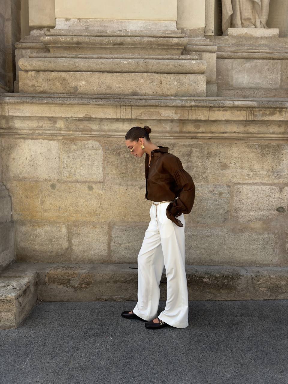 Woman in a brown jacket and white pants standing on stone steps.