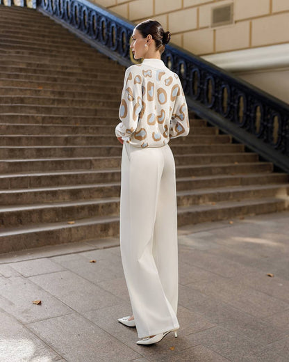 Woman in a patterned blouse and white pants standing on steps outdoors