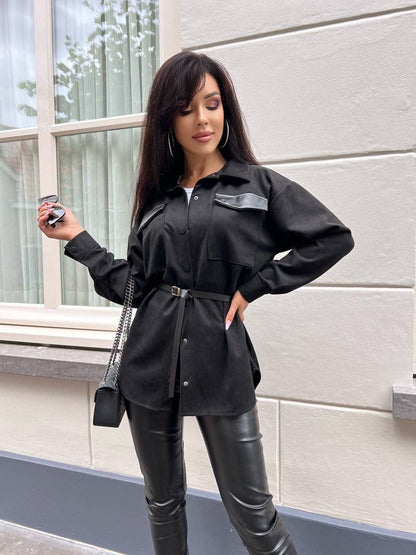 Woman wearing a black outfit with a belt, standing against a light-colored wall.