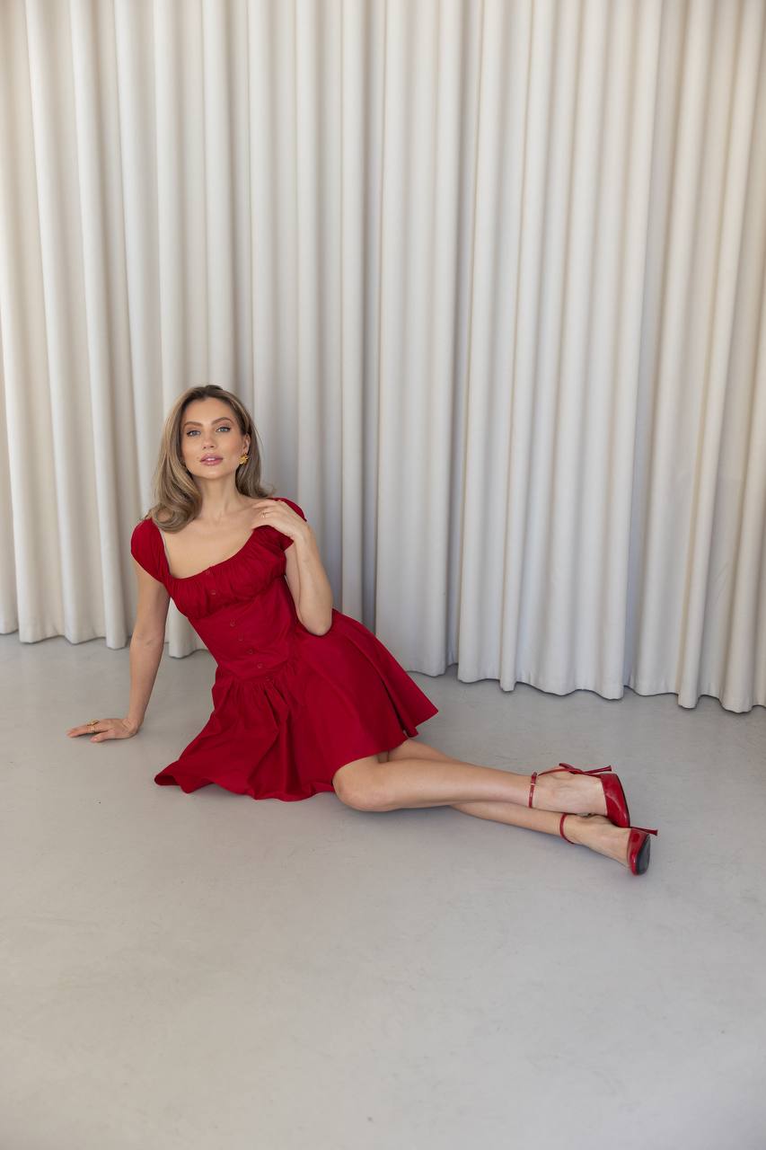 Woman in a red dress posing against a white curtain