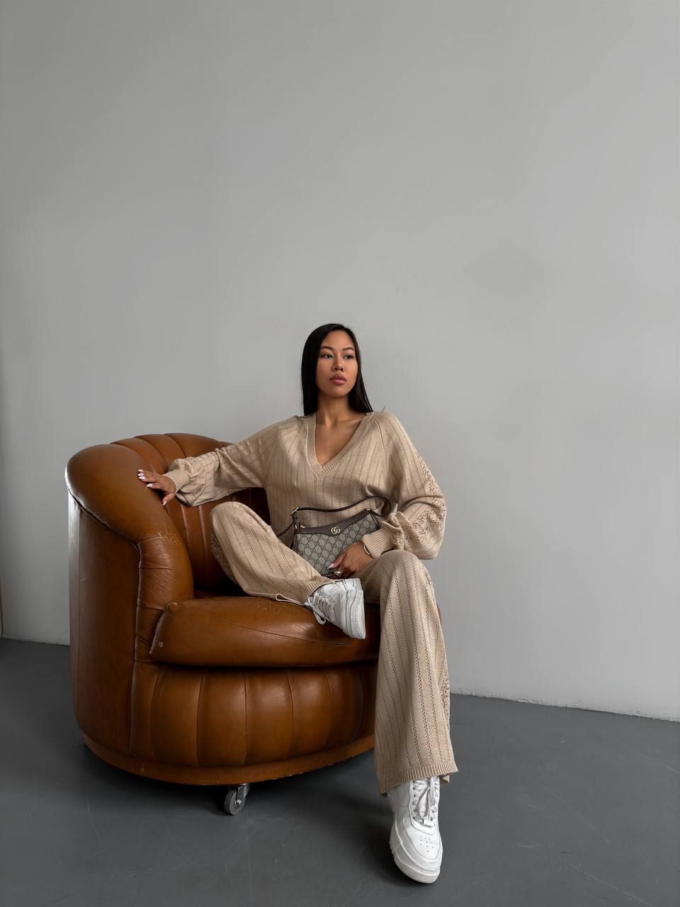 Woman sitting on a brown leather armchair against a gray wall