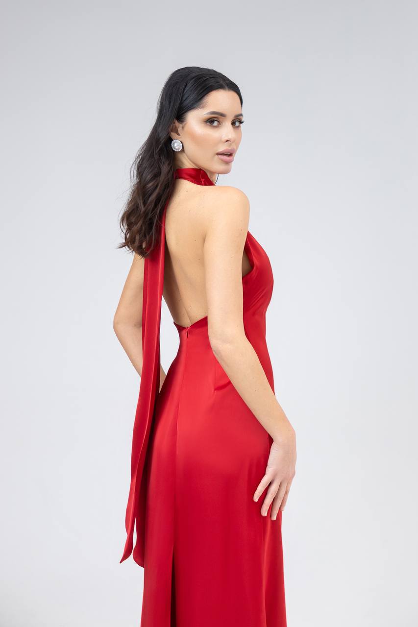 Woman wearing a red halter neck dress with a long train on a plain background