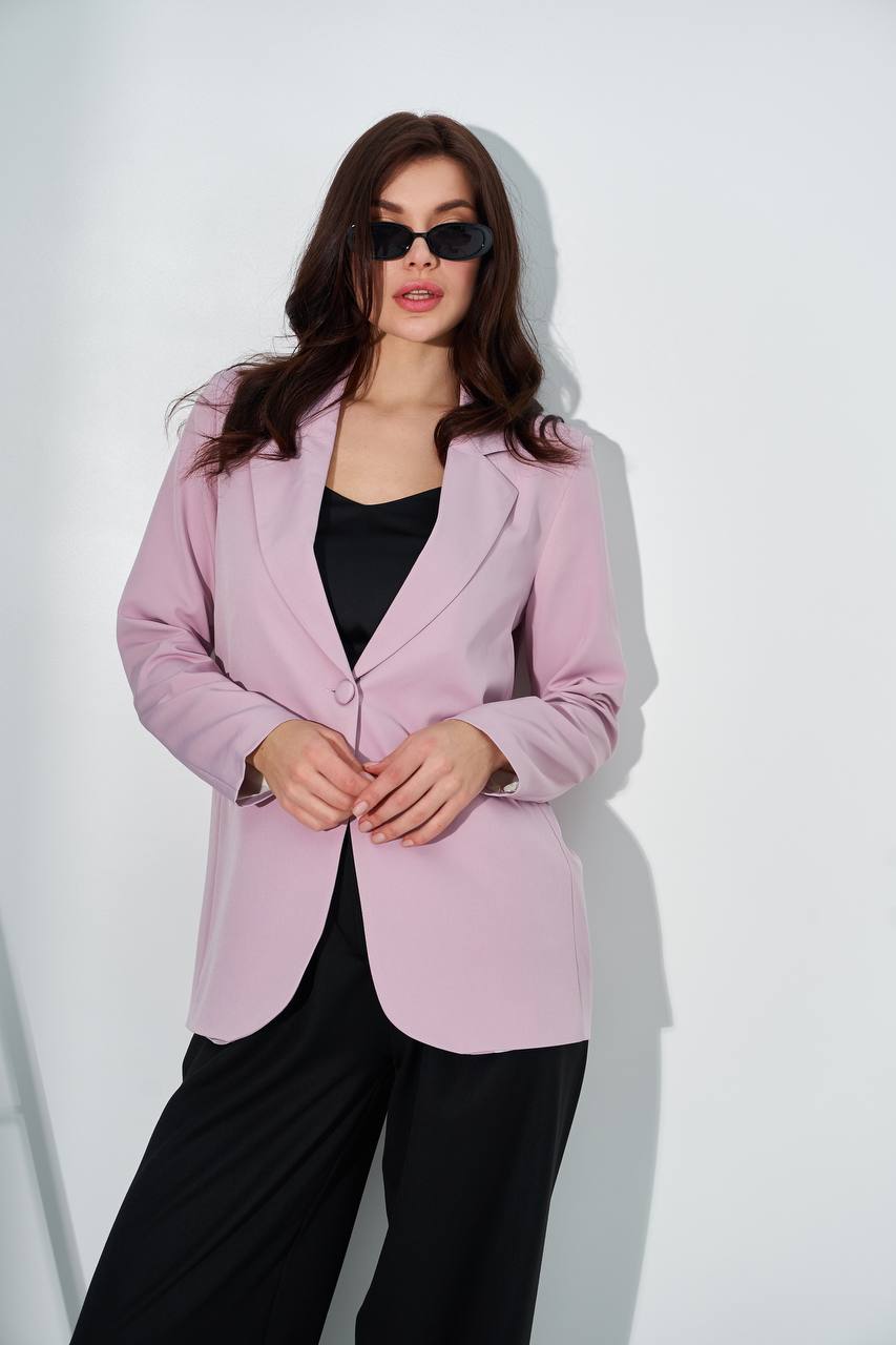 A woman modeling a light pink blazer over a black top and black wide-leg pants, standing against a plain white wall.