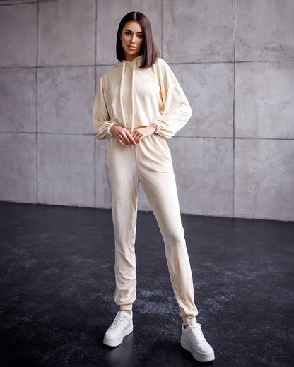 Person wearing a beige tracksuit against a gray wall.