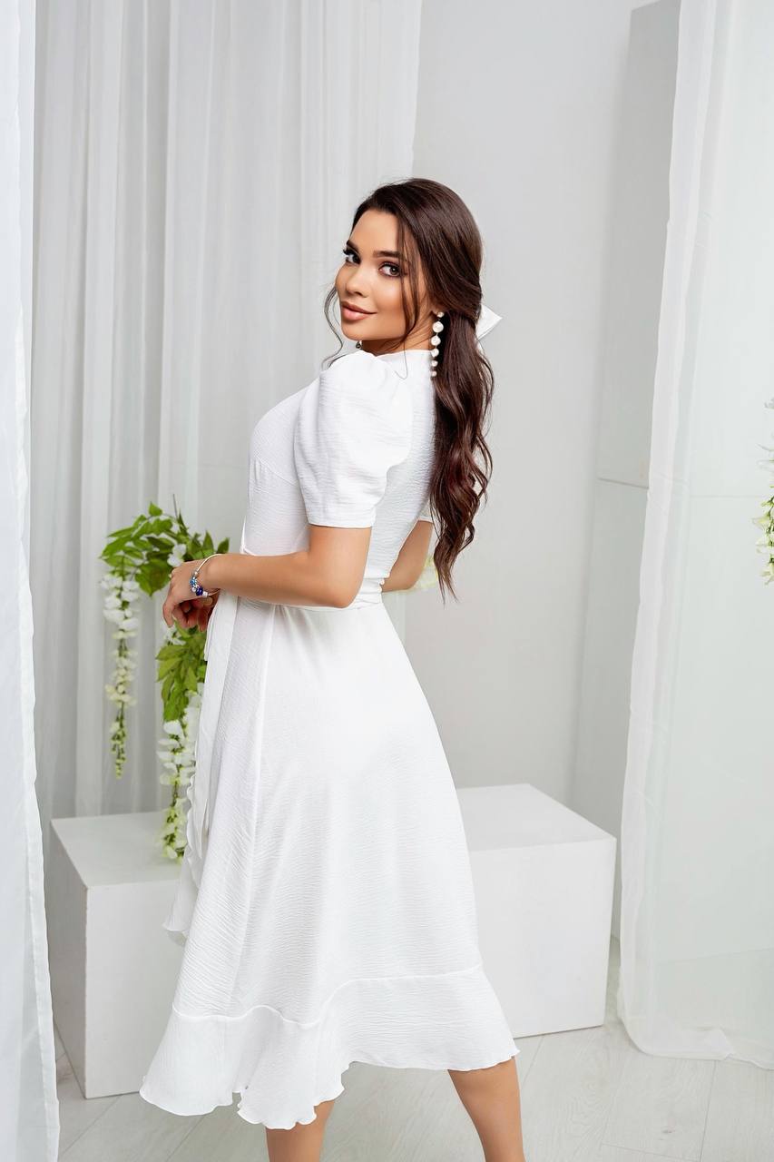 Woman in a white dress standing in a bright room with white curtains.