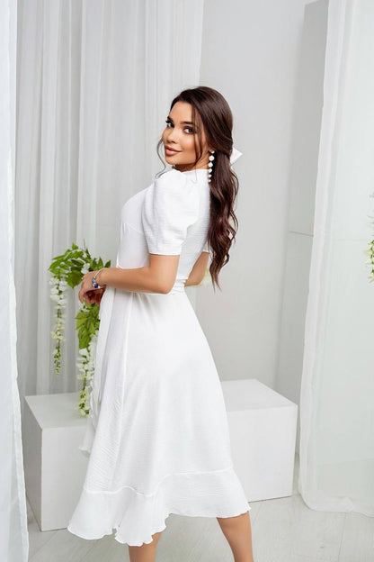 Woman in a white dress standing in a bright room with white curtains.
