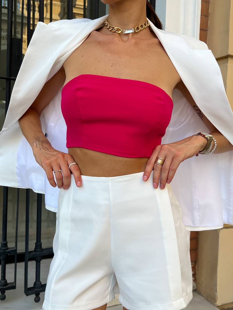 Person wearing a bright pink strapless top and white pants outdoors.