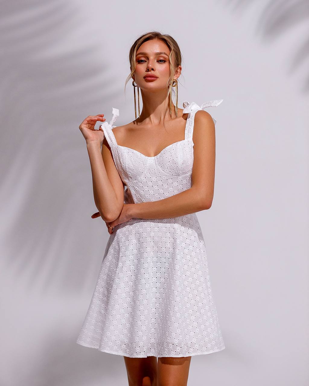 Woman wearing a white dress with floral patterns against a plain background