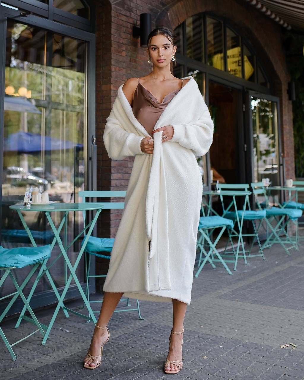 Woman in a white cardigan and brown top standing in an outdoor cafe setting