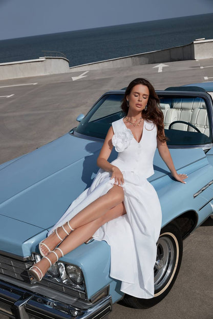 Woman in a white dress sitting on a classic blue car by the sea.