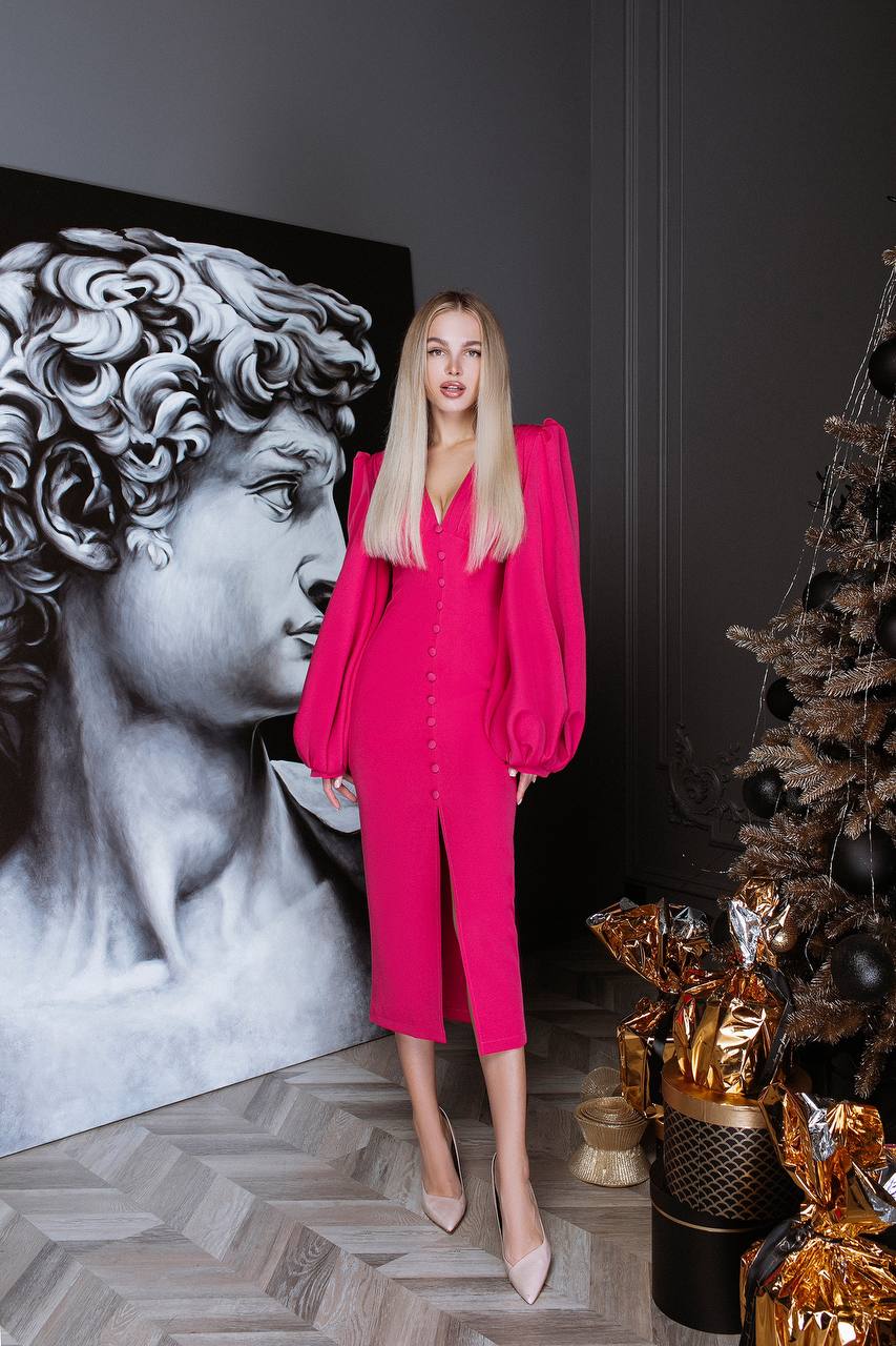 Woman in a bright pink outfit standing in a room with a classical sculpture and Christmas tree.
