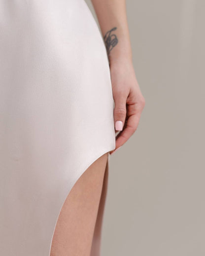 Person wearing a white dress with a cutout design, holding the hem with a neutral background.