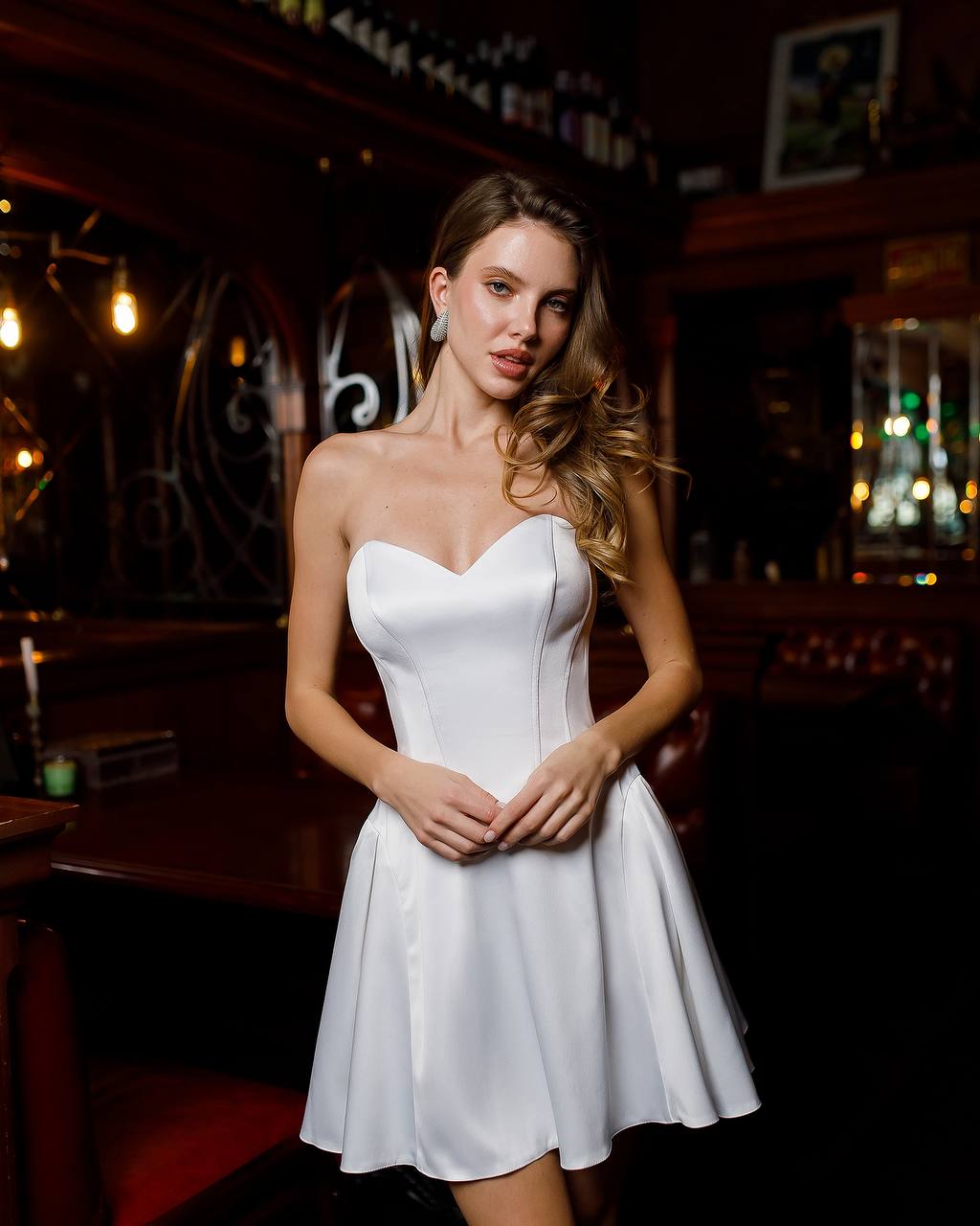 Woman in a white dress standing in a dimly lit bar.