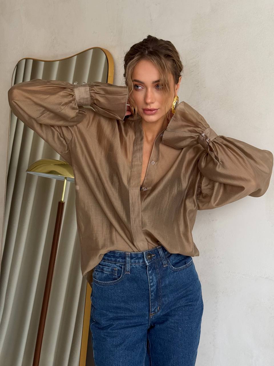 Woman wearing a brown satin blouse and blue jeans against a neutral background
