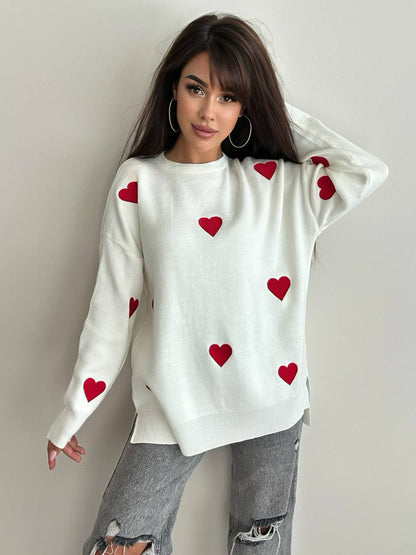 Woman wearing a white sweater with red heart patterns against a plain background