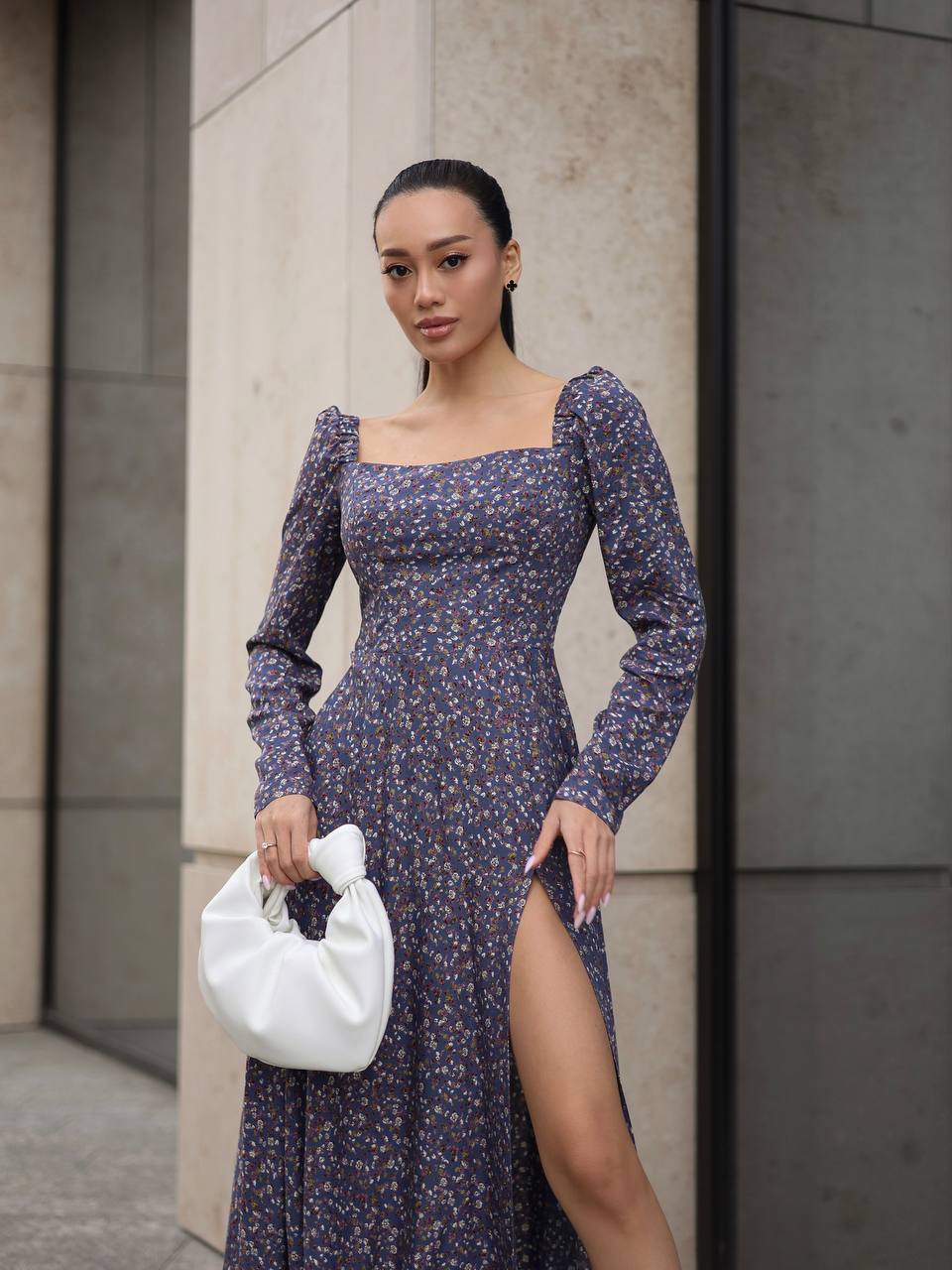 Woman in a floral dress holding a white handbag against a neutral background