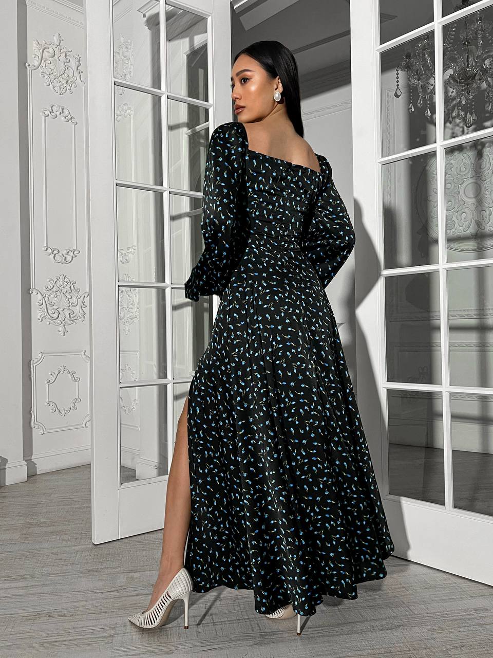 Woman in a black floral dress standing in a room with white walls and large windows.
