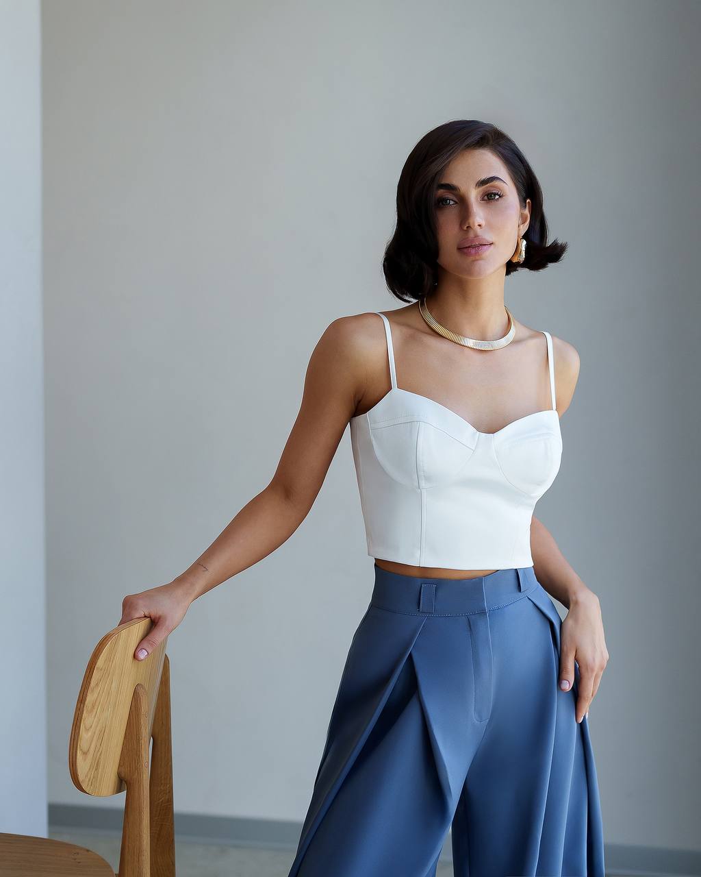 Woman wearing a white top and blue pants against a plain background