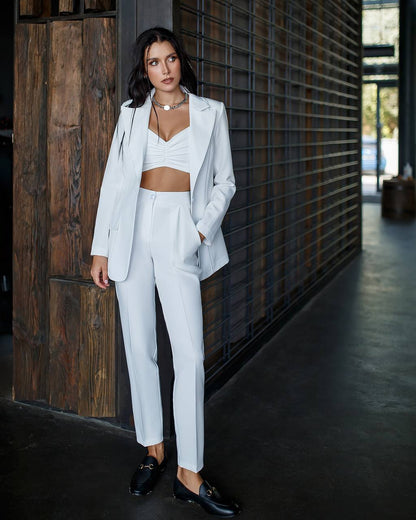 Woman in a white suit standing against a wooden wall.