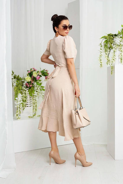 Woman in a beige dress holding a handbag in a minimalistic setting with plants.
