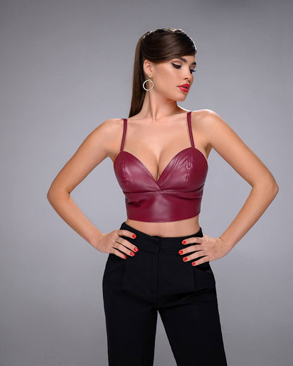 Woman wearing a burgundy leather top and black pants on a gray background