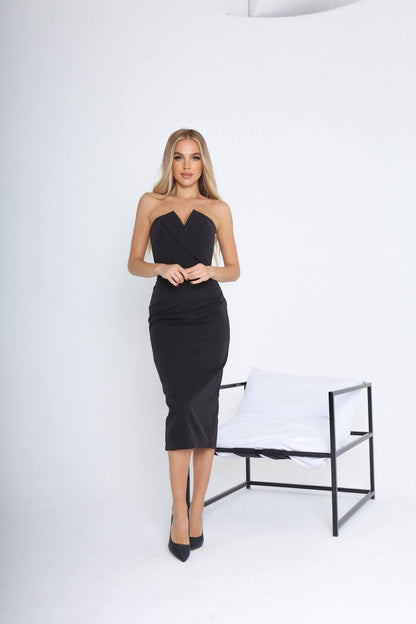 Woman wearing a black strapless dress standing in a minimalistic setting with a white chair.