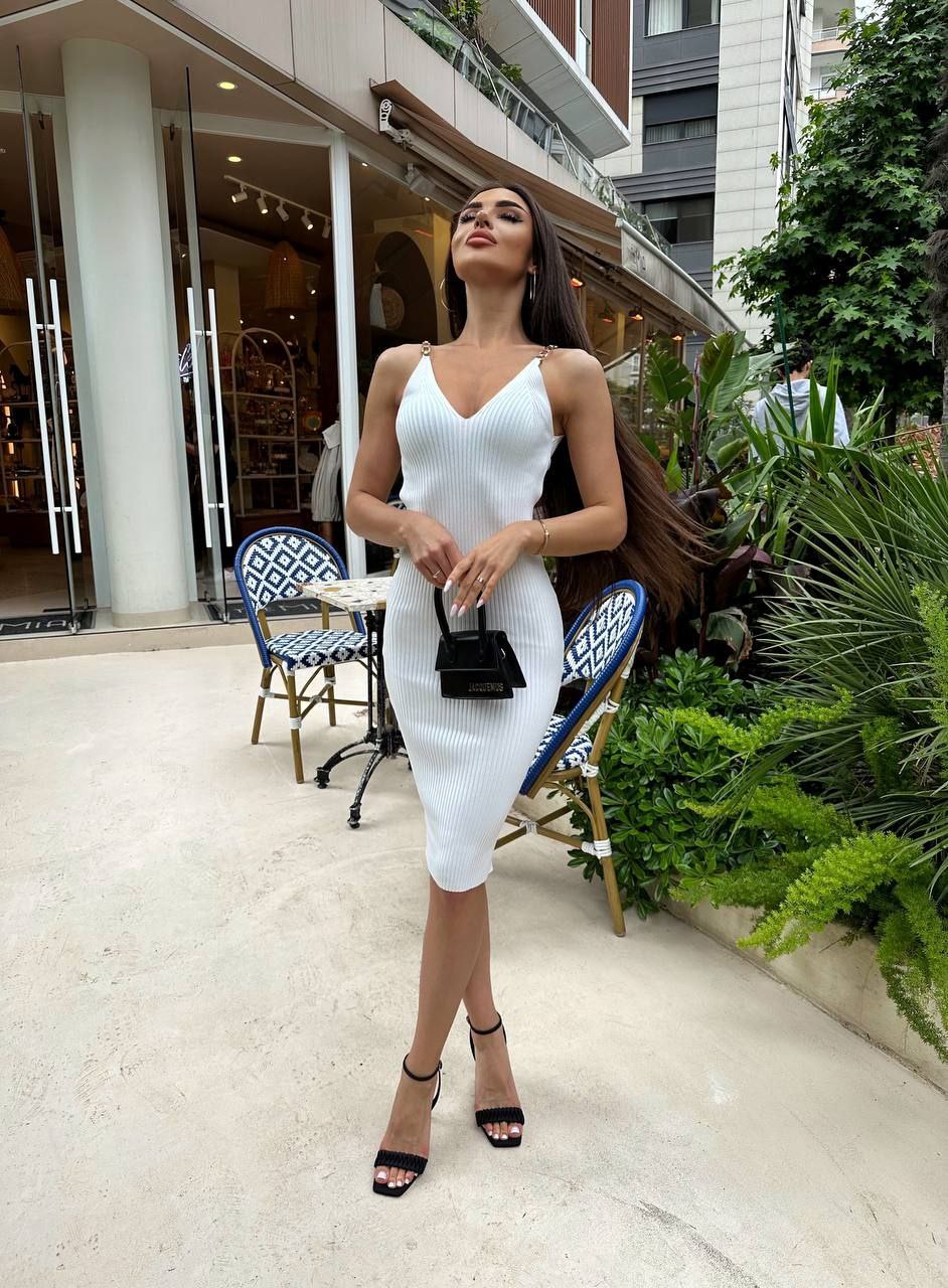 Woman in a white dress standing outdoors with a building and plants in the background