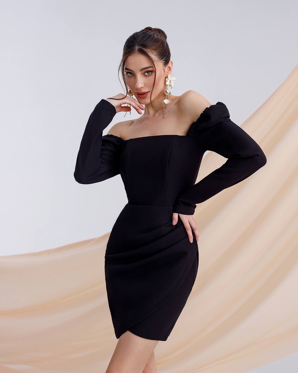 Woman wearing a black off-shoulder dress with long sleeves against a neutral background