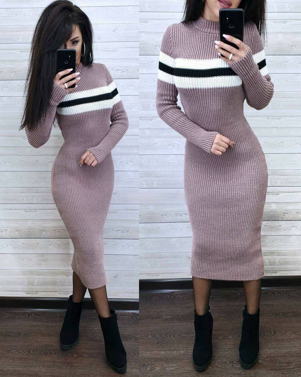 Woman wearing a pink ribbed knit dress with black and white stripes, standing in front of a wooden panel wall.