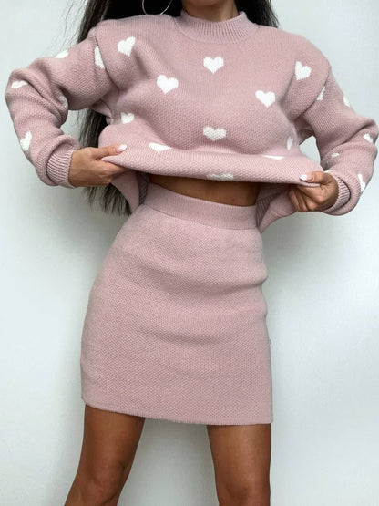 Person wearing a pink sweater and skirt set with heart patterns on a white background